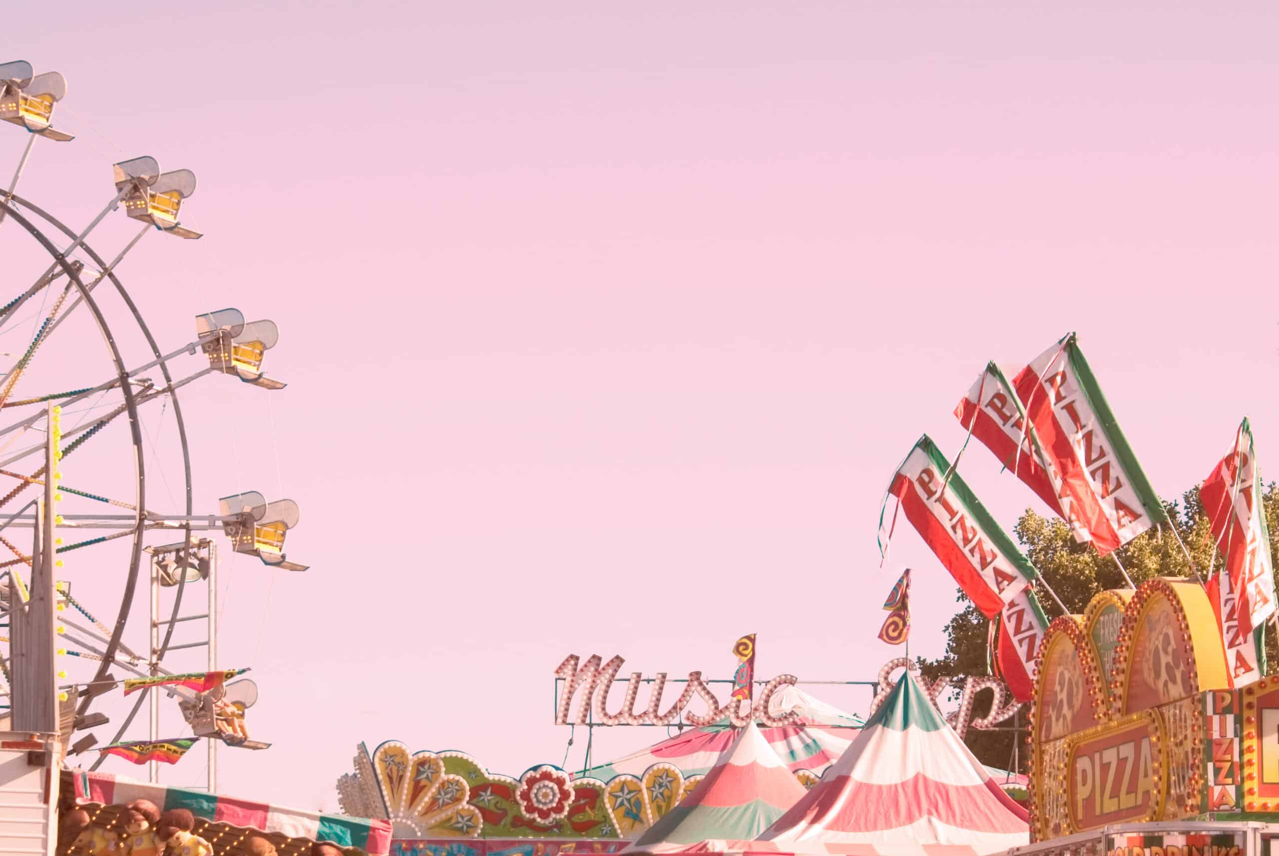 Partial view of a carnival: a large Ferris wheel on the left and colorful striped tents with flags on the right.