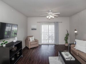 Living room with a white ceiling fan, dark wood floor, wall-mounted TV, sliding door with vertical blinds, and plants.